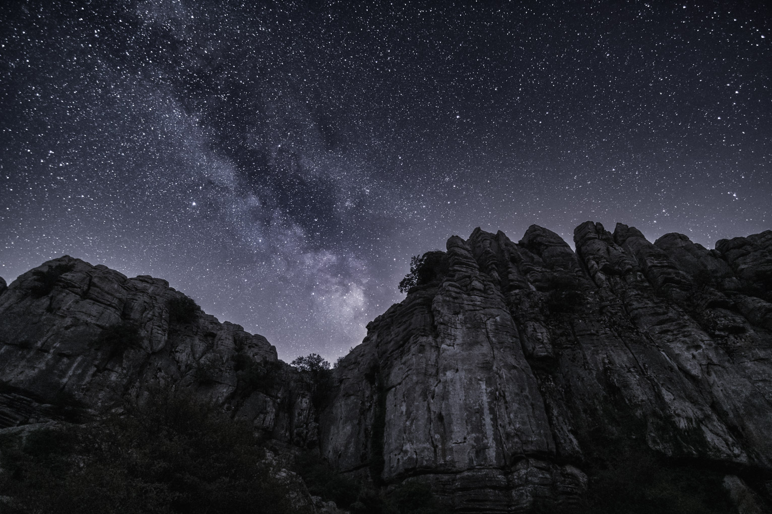 The Milky Way rises up over rocky cliffs